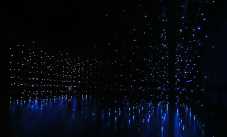 Dark room filled with countless small blue lights, some hanging from the ceiling and others reflecting off the shiny floor, creating a mesmerizing, starry, immersive space—nowiswhenweare the stars.
