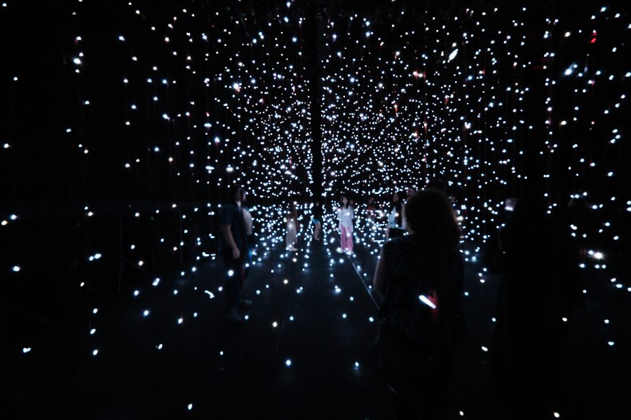 People walk through a dark room filled with suspended points of white light, creating a starry, immersive installation art experience—nowiswhenweare the stars.