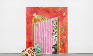 A colorful abstract painting with pink, red, and orange stripes, geometric shapes, and a mix of patterns, sits against a white wall with a painted ceramic piece featuring red dots and blue curves placed in front.