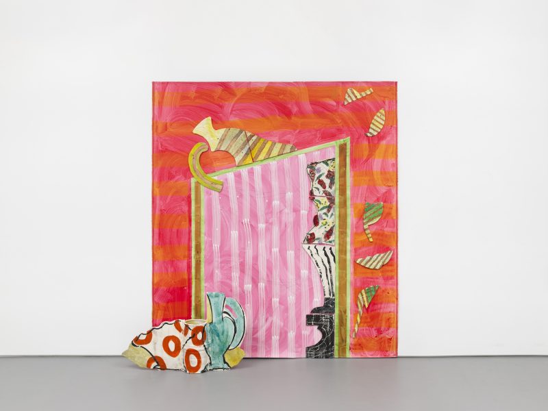 A colorful abstract painting with pink, red, and orange stripes, geometric shapes, and a mix of patterns, sits against a white wall with a painted ceramic piece featuring red dots and blue curves placed in front.