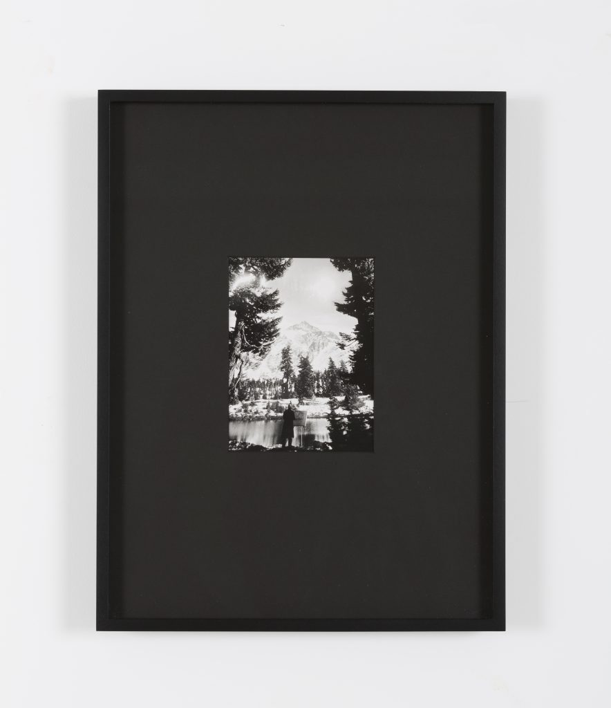 A small black and white landscape photo of a mountain and trees is centered in a large black frame with a wide mat, displayed against a white background.
