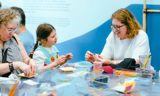 Three people sit at a table doing arts and crafts with colorful string and paper.