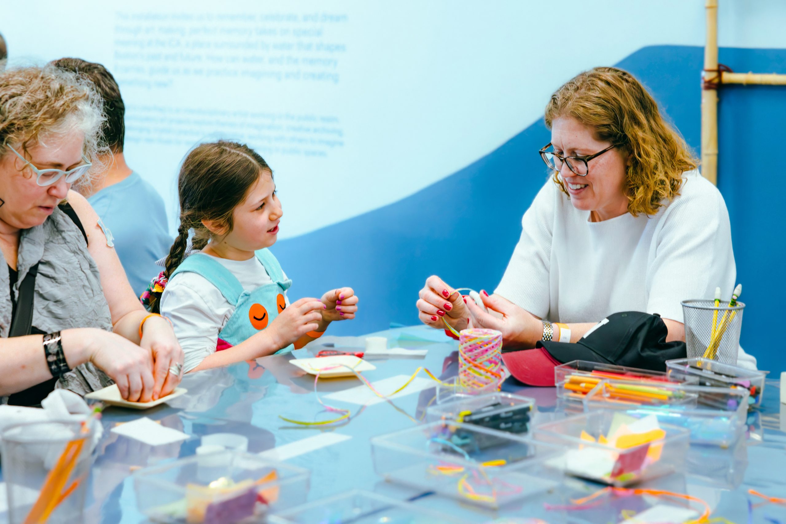 Three people sit at a table doing arts and crafts with colorful string and paper.
