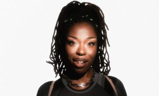 A woman smiles softly against a white background, lit dramatically from the front.