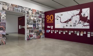 Museum exhibition gallery featuring a wall covered in photo collages, a 90 Years title, a large map of Boston with historic site markers, and smaller framed photographs with descriptive captions.