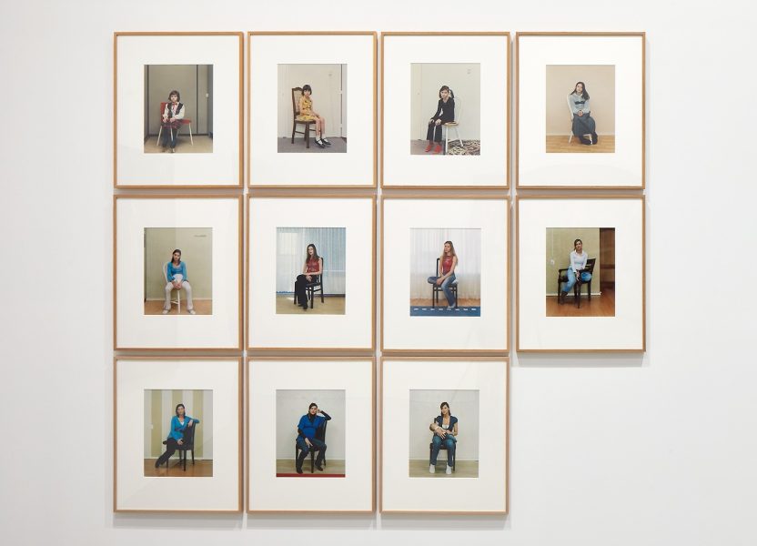 Eleven framed portraits of a woman sitting on a chair, arranged in a grid on a white wall.