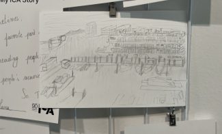 A pencil sketch of a harbor with a large cruise ship docked at a pier, displayed on a wire grid among other papers for my ica story.